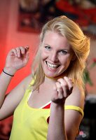 Blonde Frau bei Fußballübertragung, Top in gelb, hebt begeistert Hände