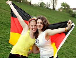 Portrait of two beautiful woman holding Germany flag behind them