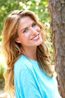 Portrait of beautiful blonde woman with long wavy hair wearing blue top, smiling