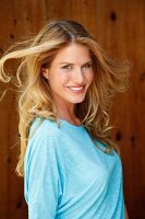 Portrait of beautiful blonde woman with windswept hair wearing blue top, smiling