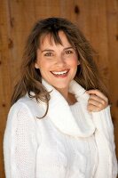 Happy woman in white turtleneck sweater standing in front of wooden wall and smiling