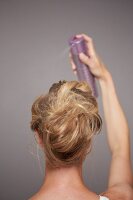 Rear view of blonde woman spraying hair spray to fix updo hairstyle