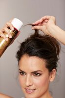 Close-up of brunette woman spraying hairspray to fix updo hairstyle, smiling
