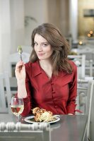 Portrait of pretty woman with brown hair in red blouse eating at restaurant, smiling