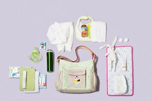 Diaper bag, changing mat and other baby care products on purple background