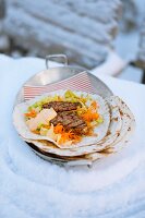 A steak wrap with a carrot and iceberg lettuce salad
