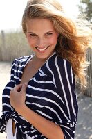 Portrait of seductive blonde woman wearing striped short coat standing on beach, smiling