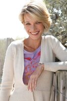 Portrait of pretty blonde woman with short hair wearing top and white cardigan, smiling