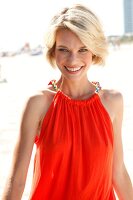 Portrait of pretty blonde woman wearing an orange top standing on beach, smiling