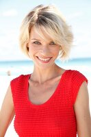 Portrait of pretty blonde woman with short hair wearing red top sitting on beach, smiling