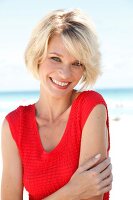 Portrait of pretty blonde woman with short hair wearing red top sitting on beach, smiling