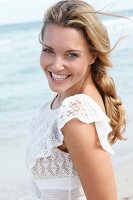 Portrait of happy blonde woman wearing white dress standing on beach, smiling