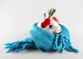 Close-up of piggy bank wrapped with blue scarf against white background