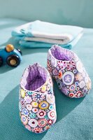 Purple homemade baby booties with flower motif on blue surface