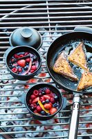 Berry compote in small pots and French toast in a pan on a barbecue