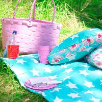 Colourful cushions and blanket with pink wicker basket in garden