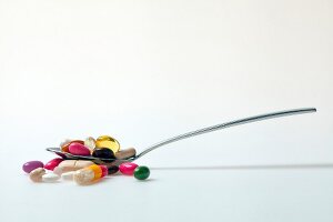 Close-up of pills, tablets, dragees and capsules in spoon against white background