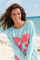 Portrait of pretty woman with dark windswept hair wearing blue top standing on beach