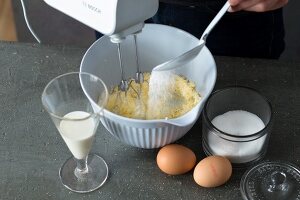 Sugar being added in mix baking ingredients in bowl for preparing waffle