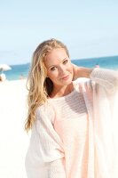 Blonde woman in a white sweater on the beach, smiling at camera