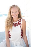 Blonde woman in a bright dress on the beach, smiling at the camera