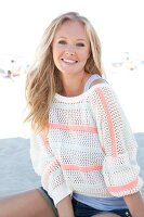 Blonde woman in a white sweater on the beach, smiling at camera
