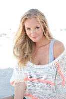 Blonde woman in a white sweater on the beach, smiling at camera