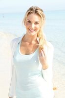 Blonde, sportliche Frau mit langen Haaren im hellen Shirt am Strand