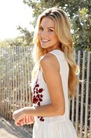 Blonde woman with long hair in a summer dress on the beach in front of a fence