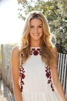 Blonde woman with long hair in a summer dress on the beach in front of a fence