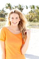 Blonde woman with long hair wearing an orange t-shirt on the beach