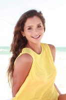 Frau mit langen dunklen Haaren im gelben Shirt am Strand