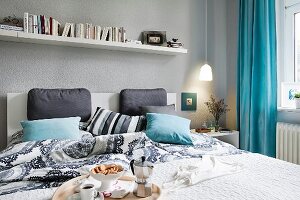 A bookshelf above a double bed with cushions and a breakfast tray