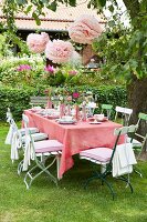 A table in a garden with a pink tablecloth and pink paper flower decorations
