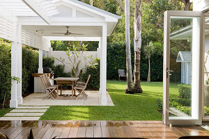 Tisch und Stühle in offenem, weißem Gartenpavillon vor Wohnhaus