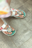 Child with flower-decorated sandals on tiled floor