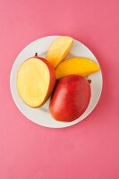Frische Mango, ganz & aufgeschnitten auf Teller (Aufsicht)