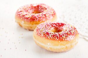 Two doughnuts with a red sugar glaze and sprinkles