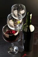 A bottle of red wine, a glass of red wine and empty wine glasses