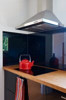 Corner of modern kitchen with reflective, black cupboard doors and red kettle on black ceramic hob
