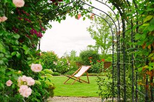 Blick auf Liegestuhl durch blühenden Rosenbogen