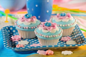 Hellblaue Cupcakes mit rosa Blüten und Zuckerperlen