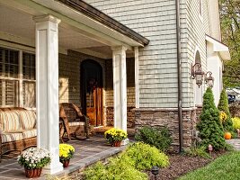 Sonnige Veranda mit gemütlichen Korbmöbeln neben der Eingangstür eines schindelbedeckten Hauses