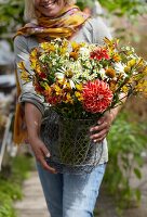 Frau trägt einen Sommerstrauss mit Dahlien, Alstroemeria, Kamille und Rudbeckia