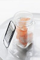A Small Open Jar of Pink Rock Salt with a Grater