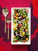 Mixed Green Salad with Red and Yellow Cherry Tomatoes and a Creamy Dressing; On a Serving Platter with Serving Spoon and Fork