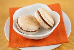 Two Dulce de Leche Macaroons in a White Bowl on an Orange Napkin