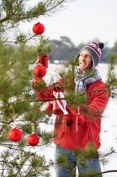 Mann schmückt einen Christbaum im Wald