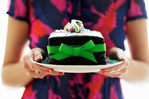 Woman Holding a Plate with a Cake Decorated with a Green Ribbon and Bow and Topped with Crushed Candy