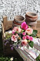 Rosenstrauss mit gestreiftem Geschirrtuch und alten Blumentöpfen in einfacher Holzkiste